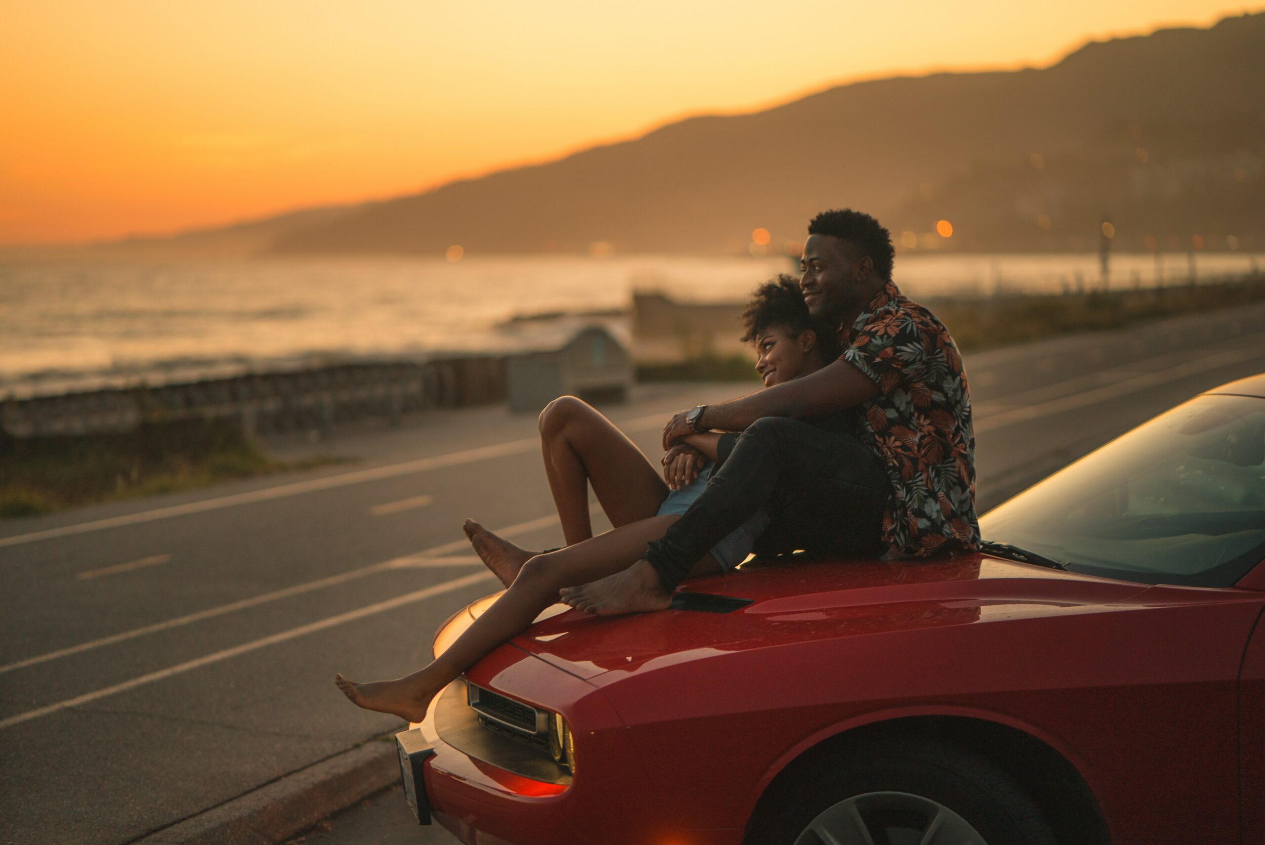 couple laughing on the hood of a car watching the sunset